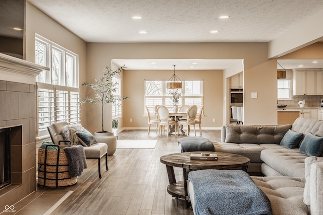 living area featuring a textured ceiling, baseboards, recessed lighting, a tiled fireplace, and light wood-type flooring