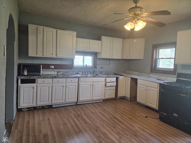 kitchen with black gas stove, a sink, white cabinets, and wood finished floors