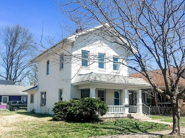 view of front facade featuring covered porch, a chimney, stucco siding, and a front yard
