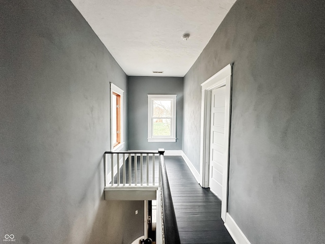 hallway featuring baseboards, dark wood-style flooring, and an upstairs landing