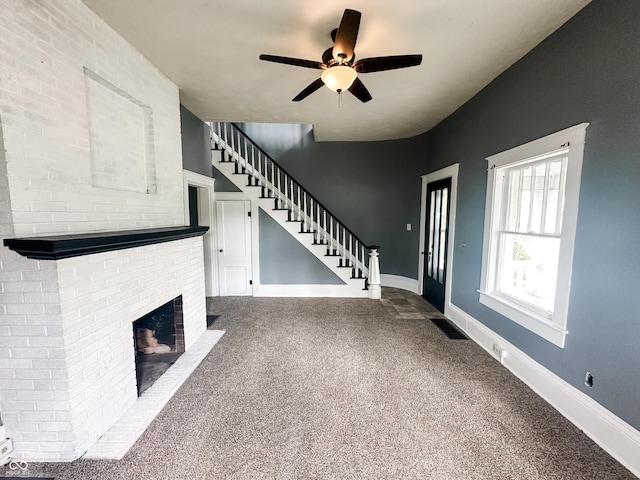 unfurnished living room with ceiling fan, visible vents, a brick fireplace, carpet, and stairs
