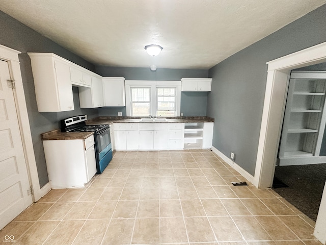 kitchen featuring light tile patterned flooring, dark countertops, range with electric stovetop, white cabinetry, and a sink