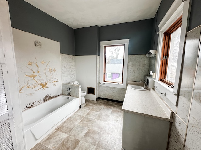 bathroom featuring vanity, a bath, a wealth of natural light, and toilet