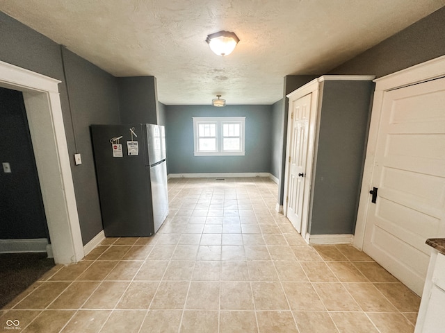 interior space featuring baseboards, a textured ceiling, and light tile patterned floors