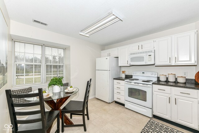 kitchen with a textured ceiling, visible vents, white appliances, dark countertops, and white cabinetry