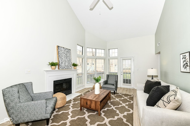 living room featuring a fireplace with flush hearth, high vaulted ceiling, wood finished floors, and a ceiling fan