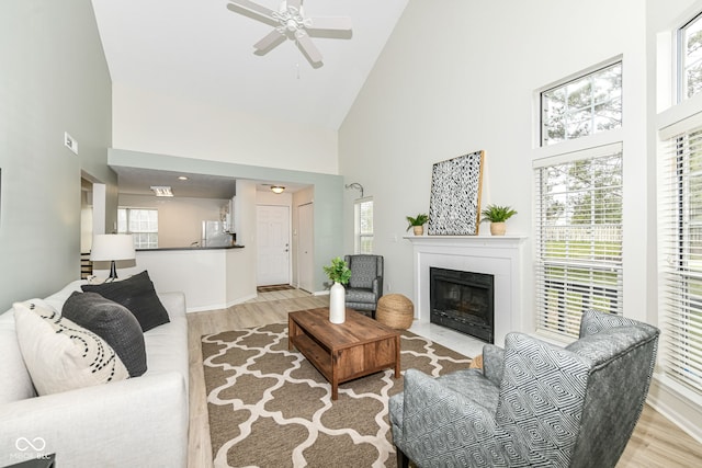 living room featuring a fireplace with flush hearth, high vaulted ceiling, wood finished floors, and a ceiling fan