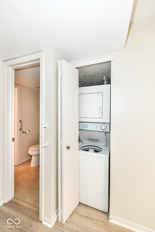 laundry room featuring a textured ceiling, stacked washing maching and dryer, laundry area, and wood finished floors