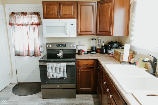 kitchen with light countertops, stainless steel electric stove, a sink, light wood-style flooring, and white microwave