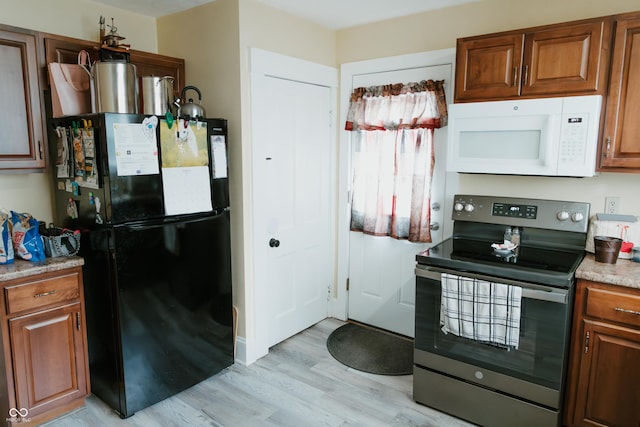 kitchen featuring freestanding refrigerator, light wood finished floors, brown cabinets, electric stove, and white microwave