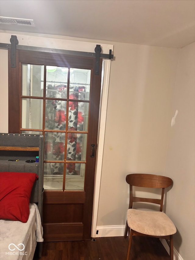 bedroom featuring visible vents, baseboards, a barn door, and dark wood finished floors