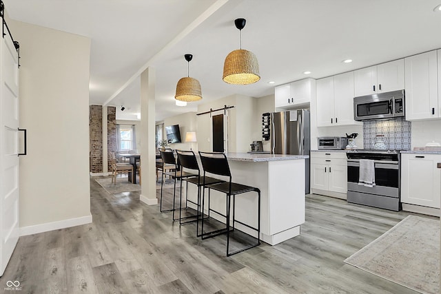 934 E Minnesota St, Indianapolis, IN 46203 - kitchen featuring a kitchen breakfast bar, tasteful backsplash, stainless steel appliances, light wood-style floors, and a barn door