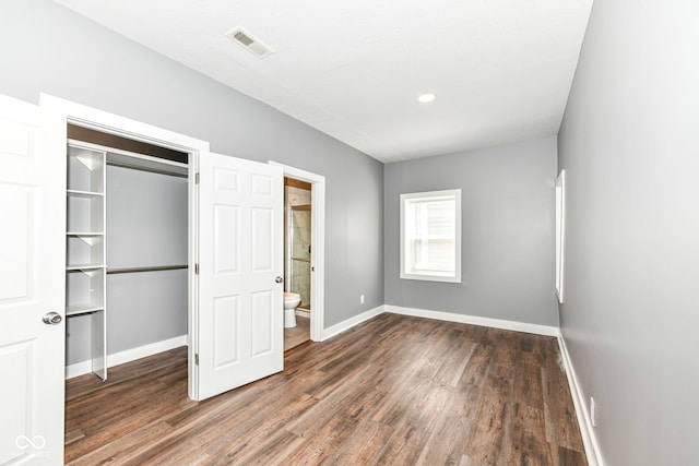 unfurnished bedroom featuring wood finished floors, a closet, ensuite bathroom, baseboards, and visible vents