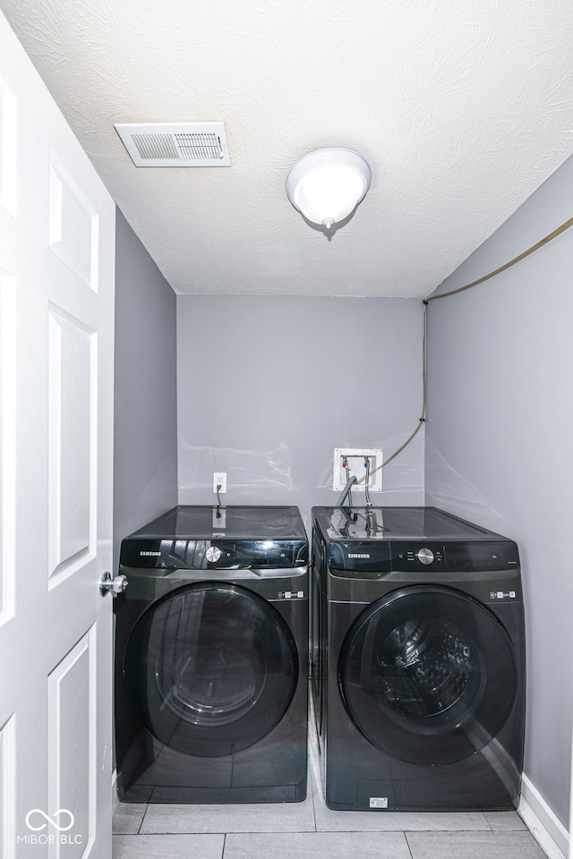 clothes washing area with visible vents, washer and clothes dryer, tile patterned flooring, and laundry area