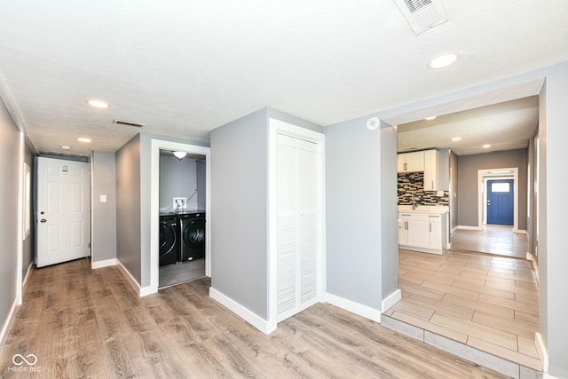 hall featuring light wood-type flooring, visible vents, baseboards, and washer and clothes dryer