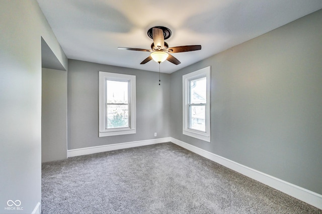 empty room featuring baseboards, dark colored carpet, and a ceiling fan