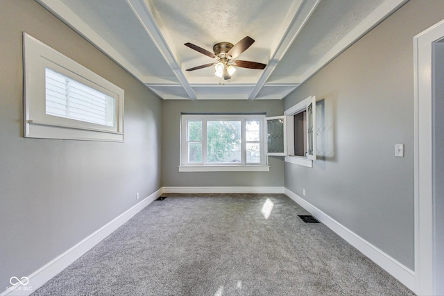 carpeted empty room with coffered ceiling, baseboards, beam ceiling, visible vents, and ceiling fan