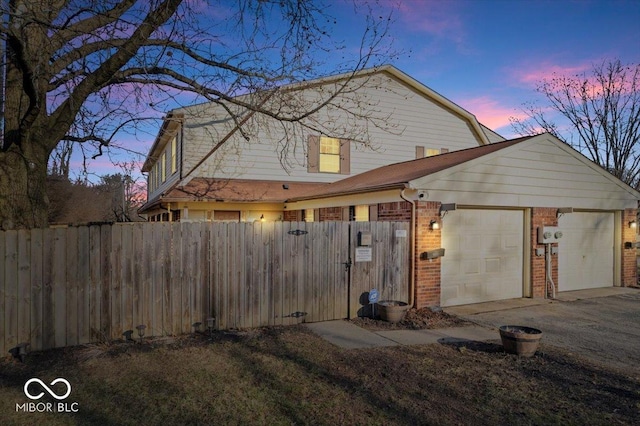 property exterior at dusk featuring brick siding, driveway, fence, and a garage