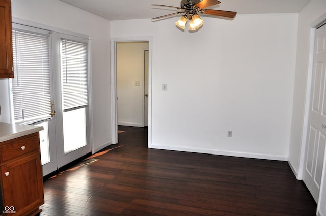unfurnished dining area with dark wood-type flooring, ceiling fan, and baseboards