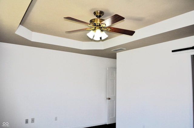 empty room with visible vents, ceiling fan, and a raised ceiling