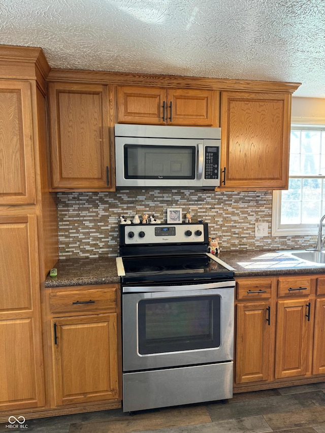 kitchen featuring backsplash, brown cabinetry, dark countertops, and stainless steel appliances