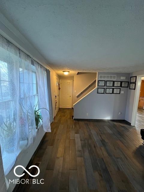 interior space featuring baseboards, stairway, dark wood-style floors, a textured ceiling, and visible vents