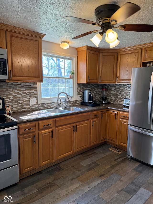 kitchen with dark countertops, brown cabinetry, appliances with stainless steel finishes, and a sink