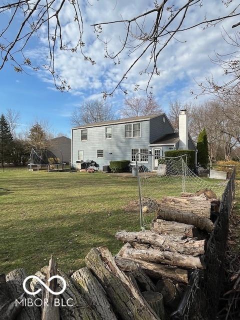 rear view of property with a trampoline, a lawn, and a chimney