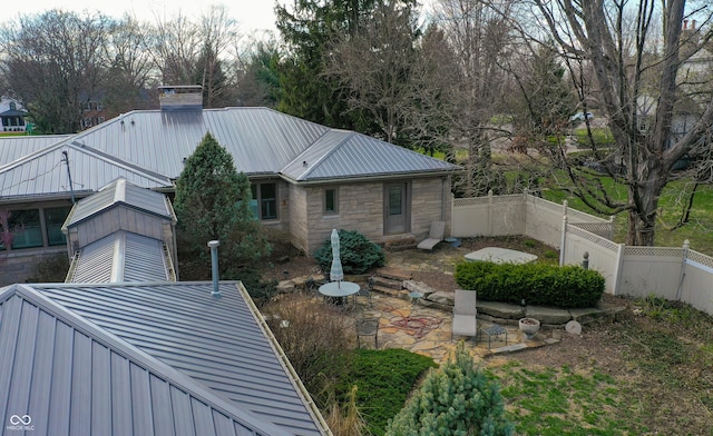 7525 N Meridian St, Indianapolis, IN 46260 - rear view of property featuring a chimney, metal roof, stone siding, a fenced backyard, and a patio area