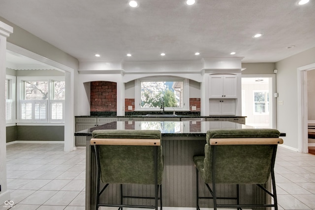 7525 N Meridian St, Indianapolis, IN 46260 - kitchen featuring a sink, white cabinetry, a kitchen bar, light tile patterned floors, and baseboards