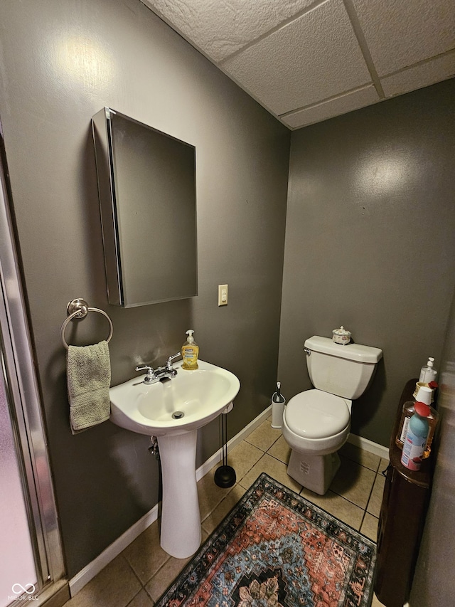 half bathroom featuring tile patterned flooring, baseboards, toilet, and a drop ceiling