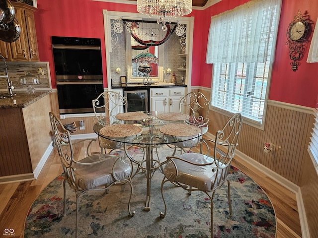 dining area featuring a notable chandelier, wooden walls, wainscoting, wood finished floors, and beverage cooler