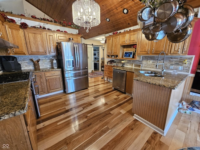 kitchen with vaulted ceiling, a barn door, appliances with stainless steel finishes, light wood finished floors, and a sink