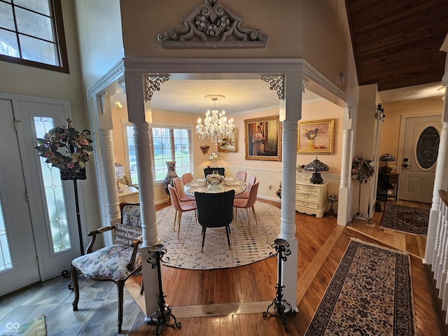 foyer entrance with a chandelier, a towering ceiling, decorative columns, and wood finished floors