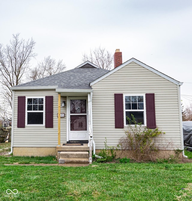bungalow-style home with a chimney, a shingled roof, and a front lawn