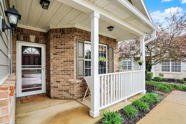 view of exterior entry featuring covered porch and brick siding