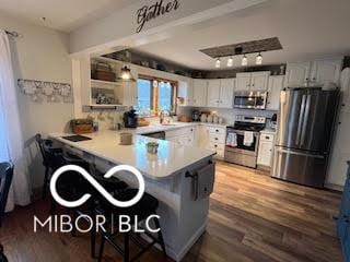 kitchen with dark wood-style floors, stainless steel appliances, a kitchen bar, a peninsula, and light countertops