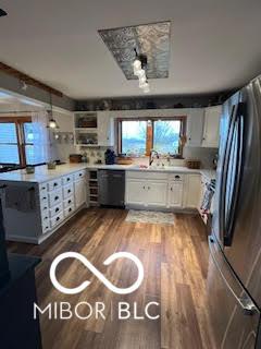 kitchen featuring wood finished floors, freestanding refrigerator, white cabinets, a sink, and dishwashing machine