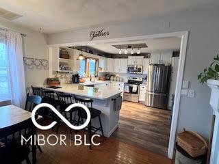 kitchen with wood finished floors, a breakfast bar area, appliances with stainless steel finishes, white cabinetry, and a peninsula