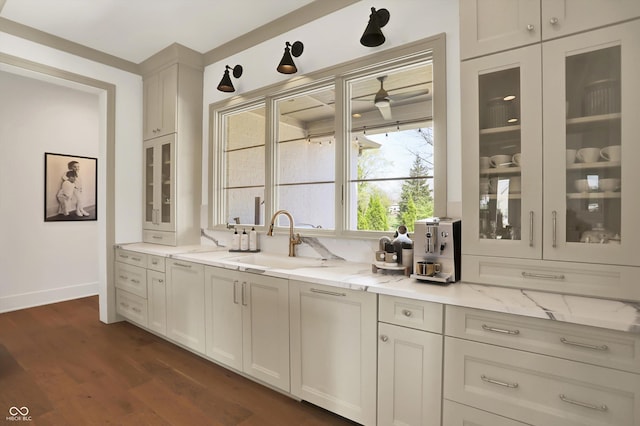 5130 Melbourne Pl, Zionsville, IN 46077 - kitchen featuring a sink, light stone counters, glass insert cabinets, dark wood finished floors, and baseboards