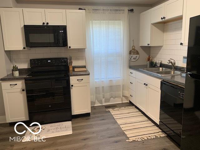 kitchen featuring white cabinetry, a sink, dark countertops, black appliances, and wood finished floors