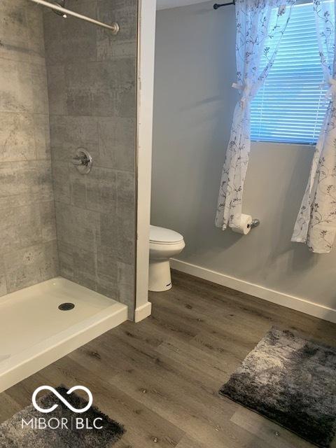 full bathroom with a stall shower, toilet, wood finished floors, and baseboards