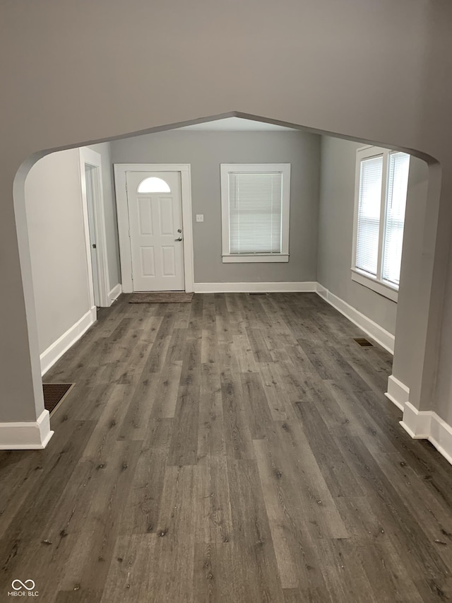 foyer with arched walkways, baseboards, visible vents, and dark wood finished floors