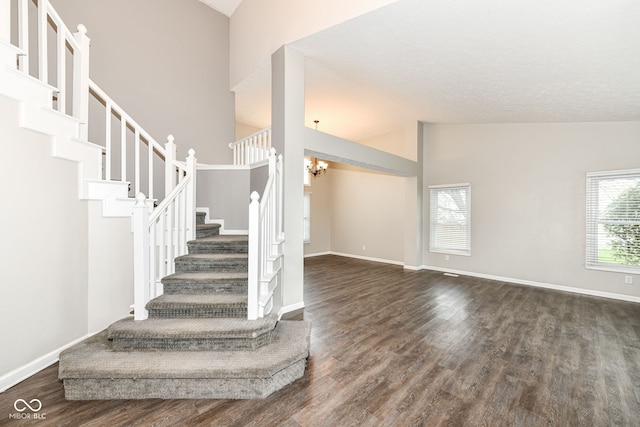 staircase featuring high vaulted ceiling, a notable chandelier, baseboards, and wood finished floors