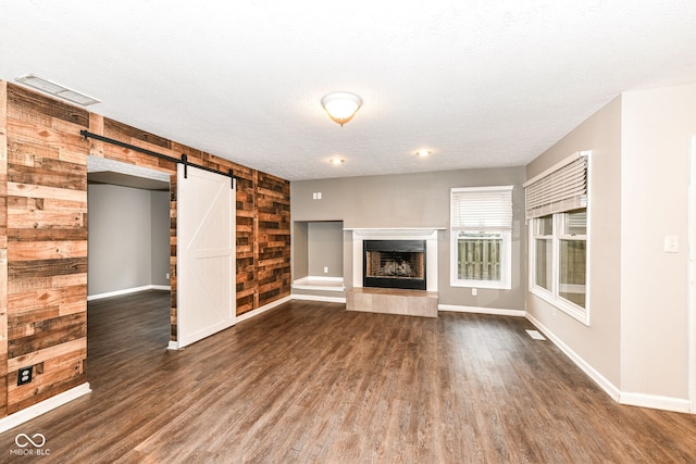 unfurnished living room with visible vents, baseboards, a barn door, dark wood-style flooring, and a textured ceiling