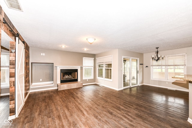 unfurnished living room featuring visible vents, baseboards, a barn door, a notable chandelier, and dark wood-style floors