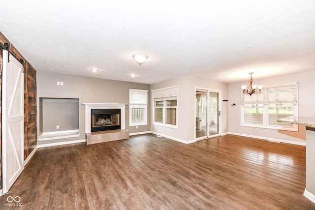 unfurnished living room featuring baseboards, a fireplace with raised hearth, a barn door, a chandelier, and wood finished floors