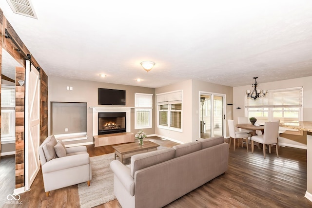 living room with baseboards, a chandelier, a barn door, visible vents, and wood finished floors