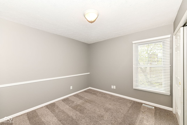 spare room featuring a textured ceiling, carpet flooring, and baseboards