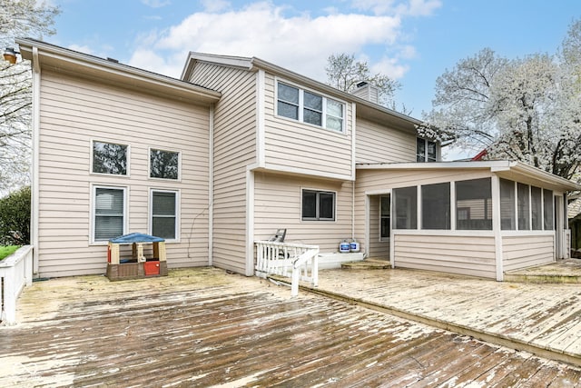 rear view of house featuring a sunroom, a chimney, and a deck